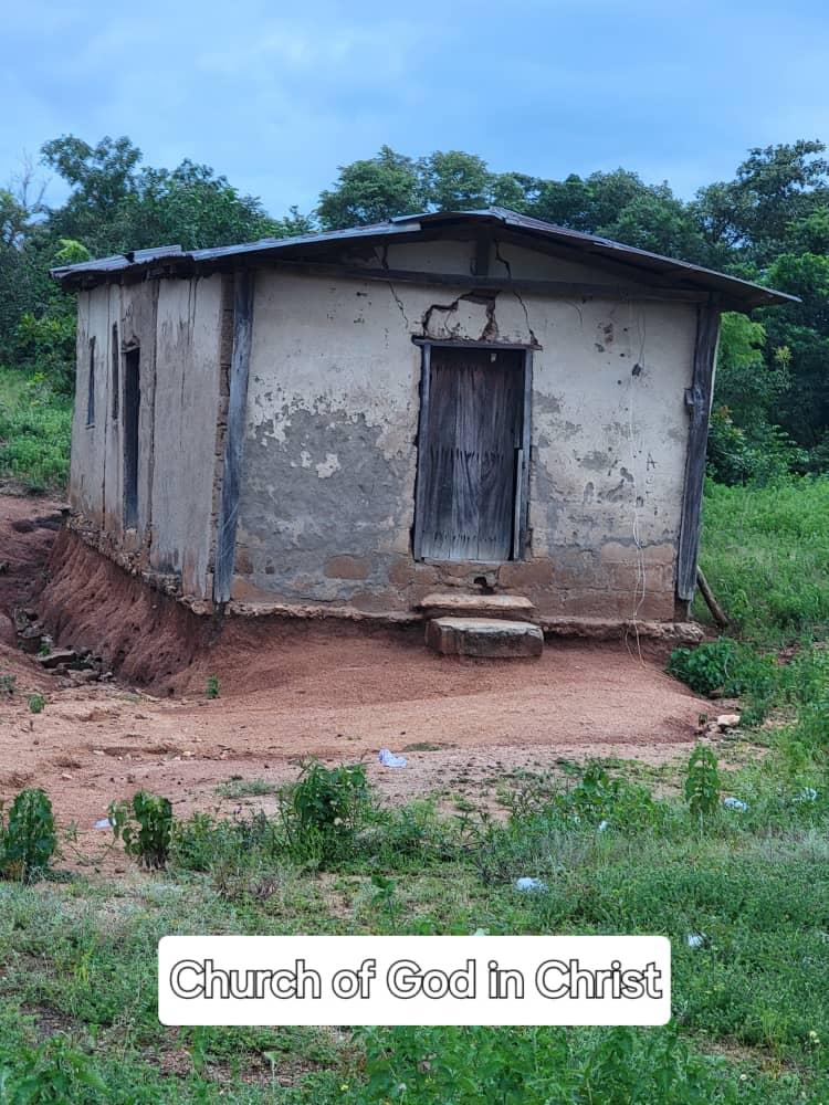 A small older church building of mud and timber construction, standing on open ground